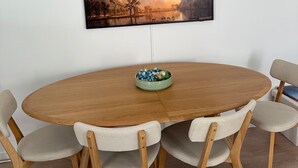 A round wooden dining table with six chairs, a framed landscape painting above it, and a bowl of snacks on the table. - Bright apartment with terrace Private parking (Rouen)