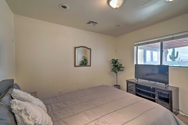 A bedroom with a bed, a TV, a window with a view of palm trees, and a plant.