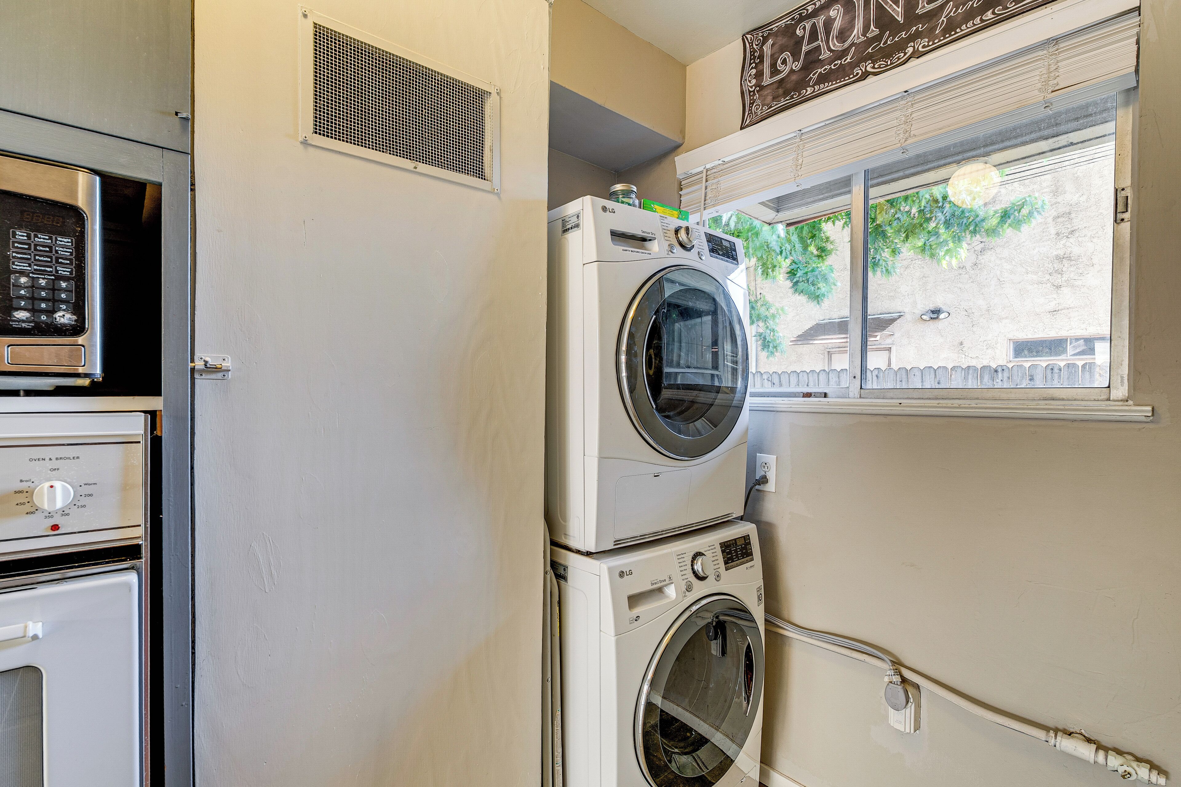 Un espace buanderie équipé d’une lave-linge et d’un sèche-linge superposés, d’un four à micro-ondes et d’une bouche d’aération.