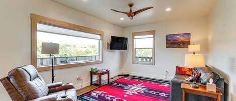A living room with a leather recliner, a colorful rug, a ceiling fan, a TV, and a couch with a lamp.