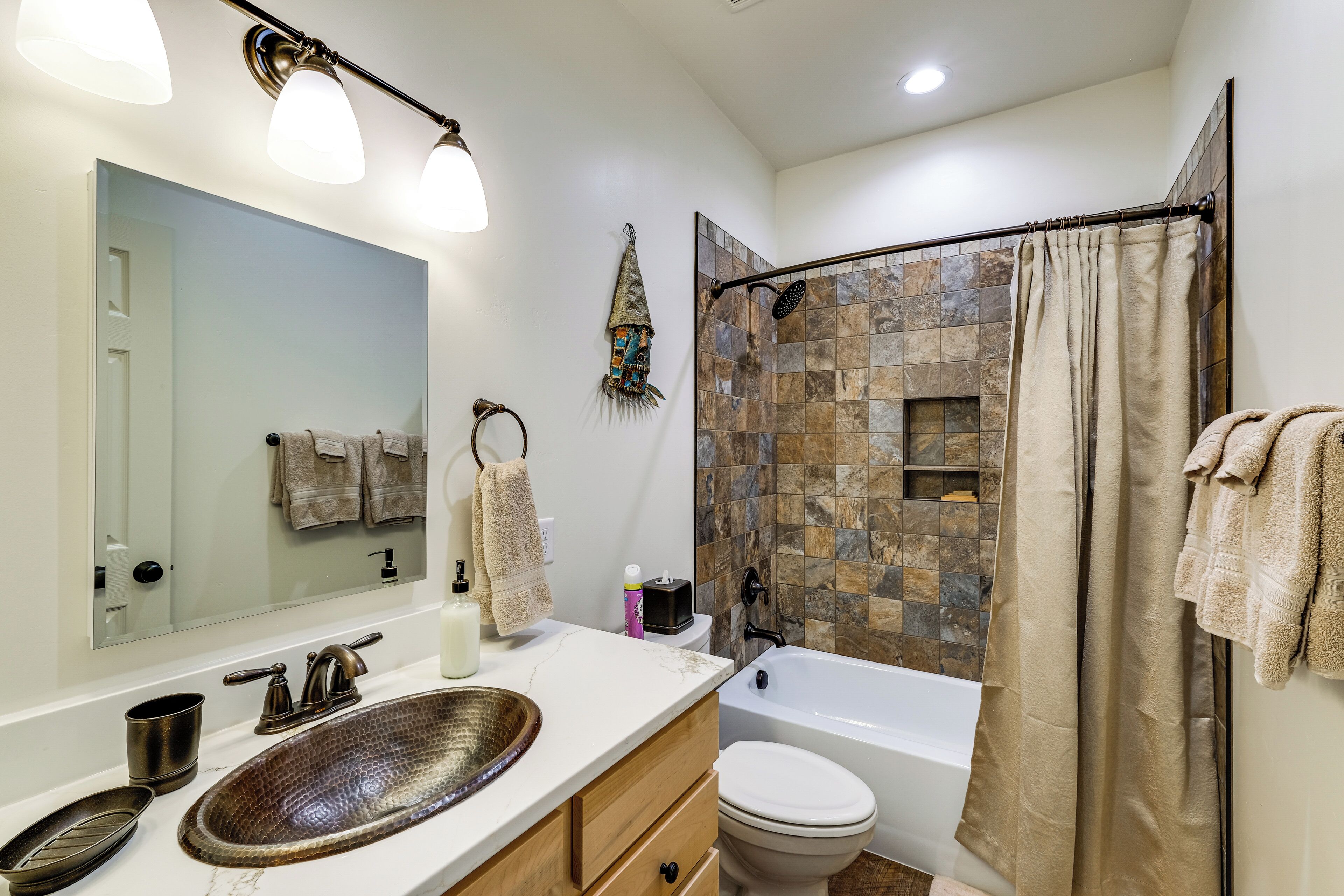 A bathroom with a large mirror, a sink with a bowl basin, a toilet, and a shower with a tiled wall.