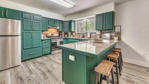 A modern kitchen with teal cabinets, stainless steel appliances, and a central island with stools. - Mountain Retreat: Near Grindstone Lake & Trails! (Ruidoso)