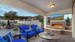 An outdoor patio with blue seating, a stone fireplace, and a TV mounted on the wall. - Breathtaking Family Retreat in Elite Gold Canyon! (Gold Canyon)