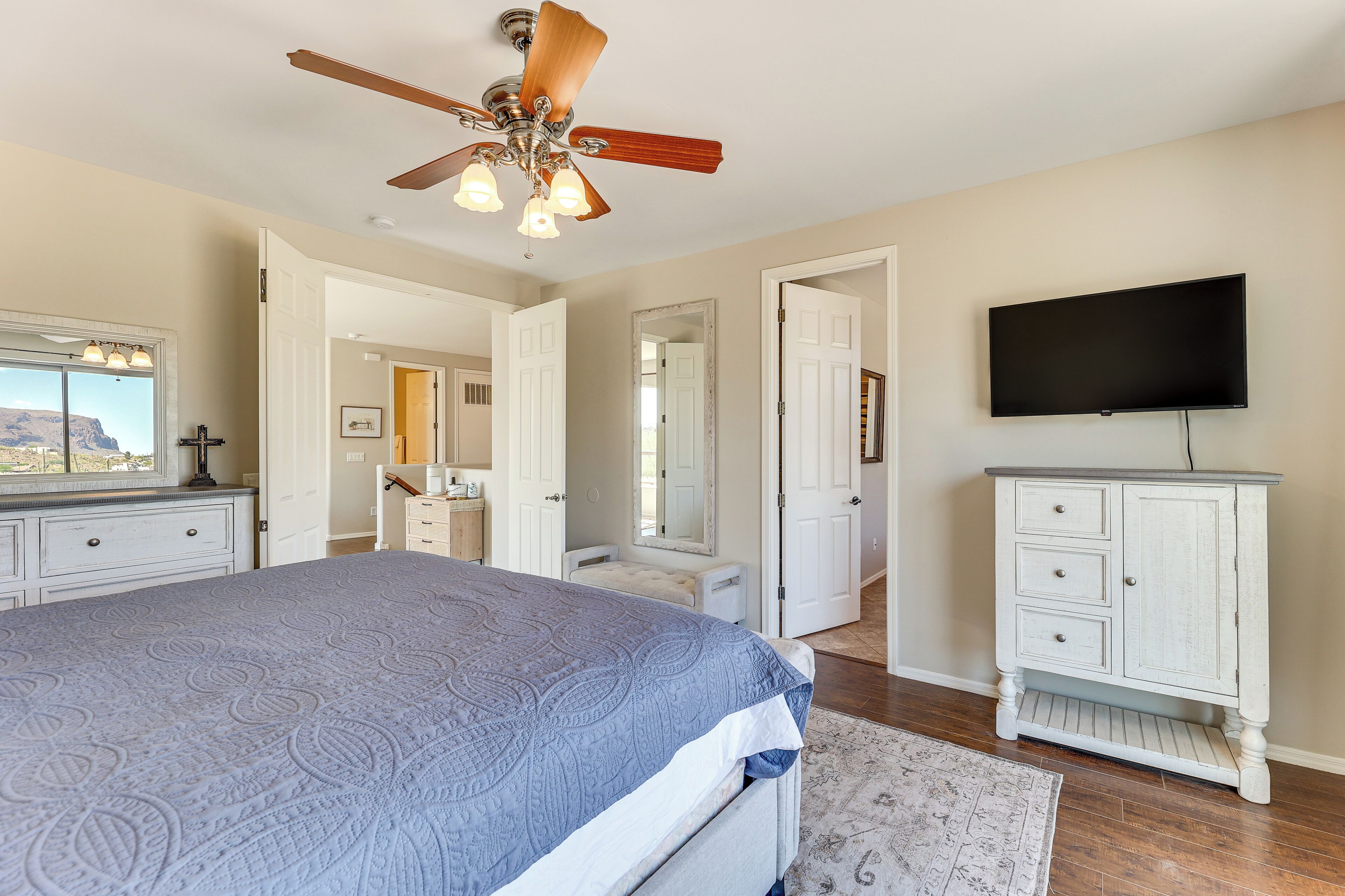 A bedroom with a bed, a ceiling fan, a television, and a dresser.