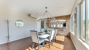 A dining area with a chandelier, round table, and chairs. There is a stone wall and a window with a view. - Breathtaking Family Retreat in Elite Gold Canyon! (Gold Canyon)