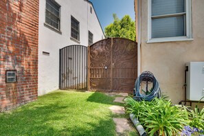 Um imóvel residencial com muro de tijolos, um edifício branco, portão de metal e um jardim com plantas e uma mangueira.