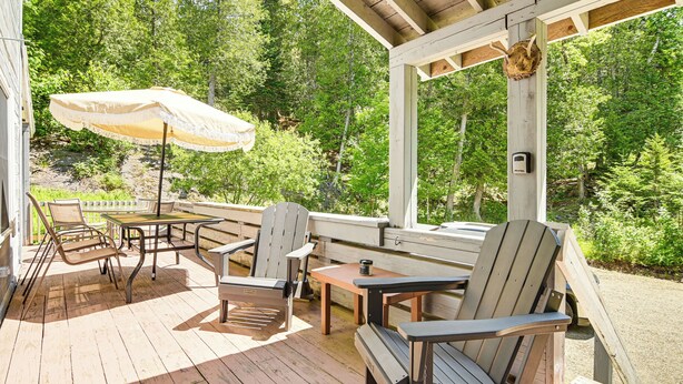 Een houten terras met buitenmeubilair, waaronder stoelen en een tafel, en een grote parasol.