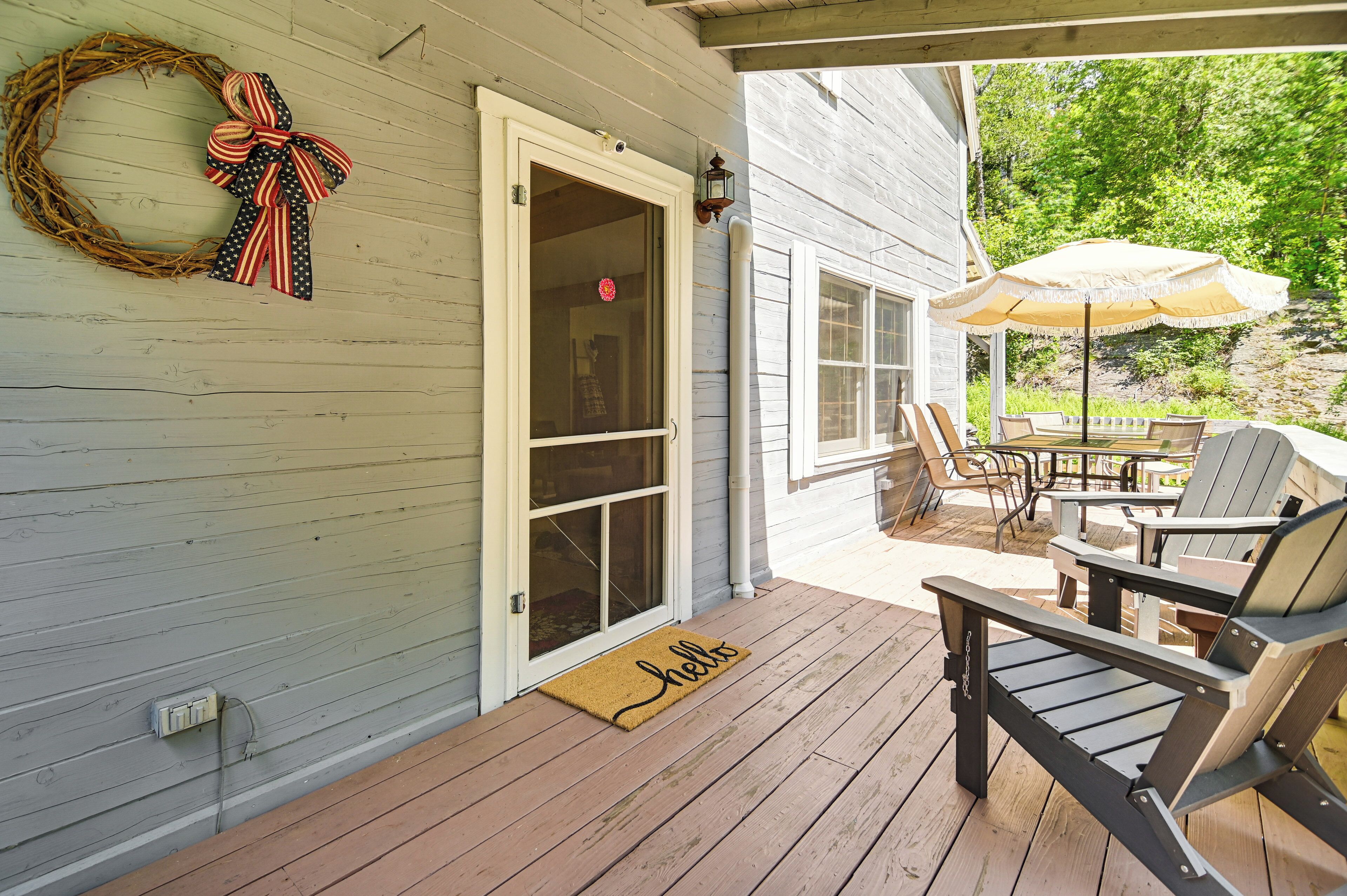 Une terrasse en bois avec des meubles d’extérieur, une porte ornée d’une guirlande et un paillasson sur lequel est écrit « Bonjour ».