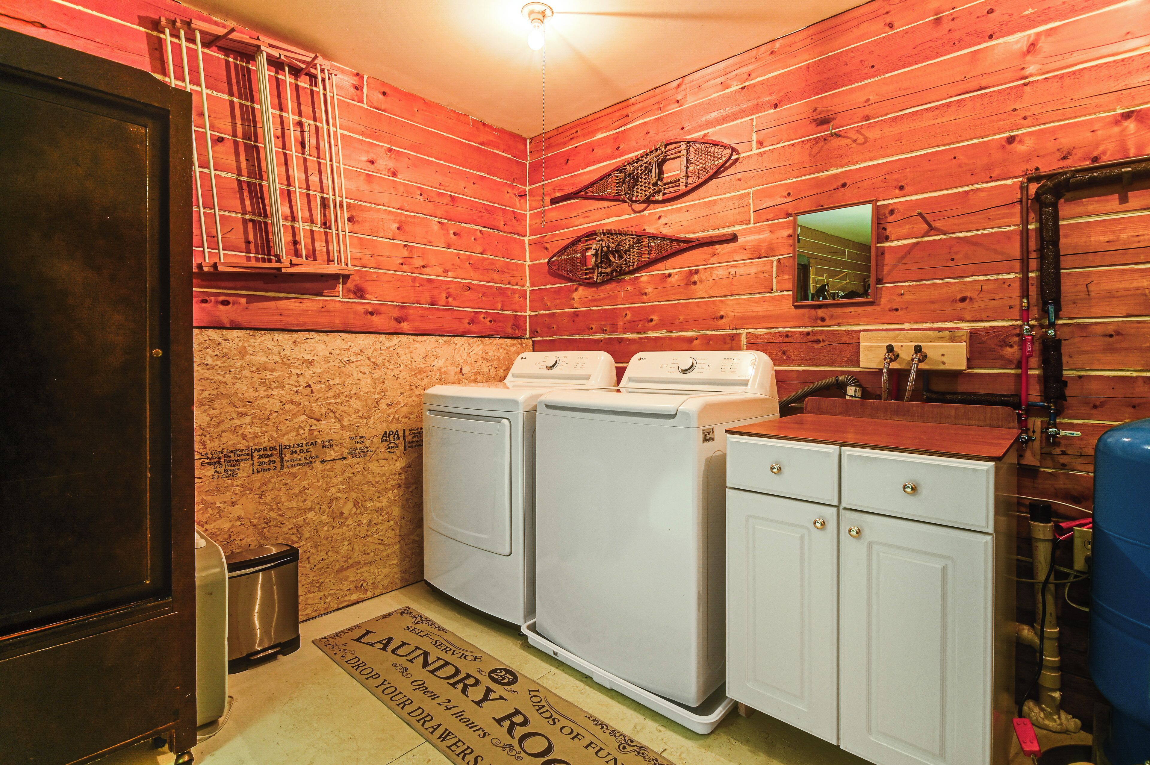 A laundry room with wooden walls, two washing machines, a sink, and a mirror.