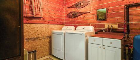 A laundry room with wooden walls, two washing machines, a sink, and a mirror.