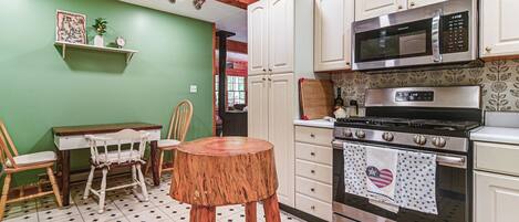 A kitchen with white cabinets, a microwave, a stove, and a dining area with a table and chairs.