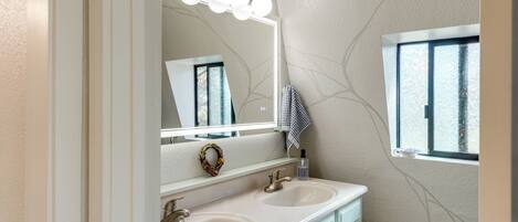 Un baño con dos lavamanos, un espejo con luces, un perchero para toallas y una ventana.