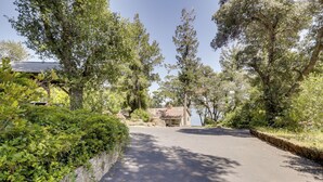 A paved driveway leading to a building with a sloped roof, surrounded by dense greenery and trees. - Boat Ramp + Dock: Waterfront Home on Clear Lake (Kelseyville)