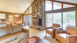 A spacious living room with a stone fireplace, leather sofas, and large windows. - Steps to White River: Cabin Retreat w/ Dock Access (Lakeview)