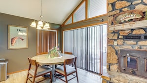 A dining area with a round table, chairs, a chandelier, a stone fireplace, and a window with blinds. - Steps to White River: Cabin Retreat w/ Dock Access (Lakeview)