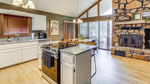 A spacious kitchen with a stone fireplace, wooden flooring, and a large island. - Steps to White River: Cabin Retreat w/ Dock Access (Lakeview)