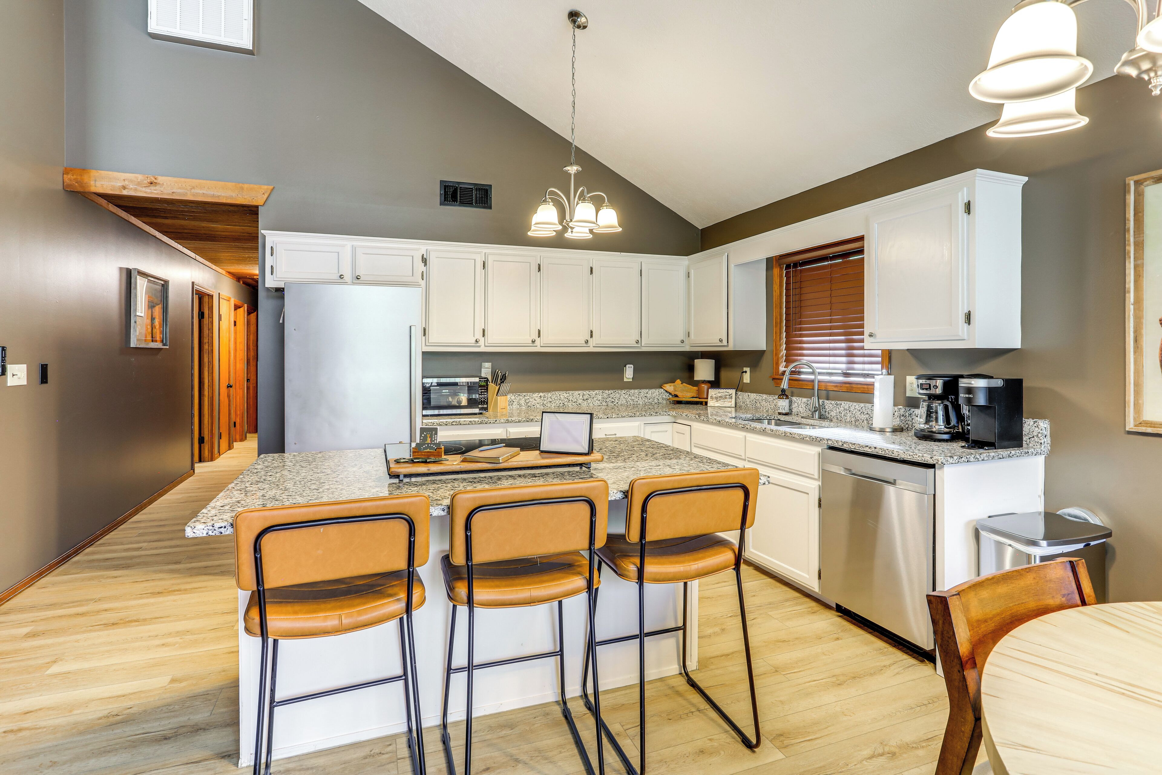 Una cocina moderna con una isla central, taburetes de bar, electrodomésticos de acero inoxidable y una lámpara colgante.