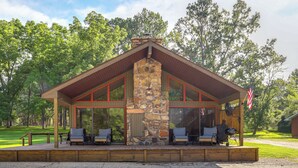 A lodge with a stone chimney, large windows, and a deck with seating. - Steps to White River: Cabin Retreat w/ Dock Access (Lakeview)
