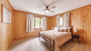 Een slaapkamer met houten wanden, een bed, een plafondventilator en een raam met gordijnen.