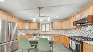 Een moderne keuken met houten kastjes, een roestvrijstalen koelkast, een inbouwoven en een eethoek met twee groene stoelen.