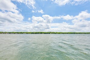Une vue sur une étendue d’eau, avec une côte lointaine, un ciel dégagé et quelques nuages épars.