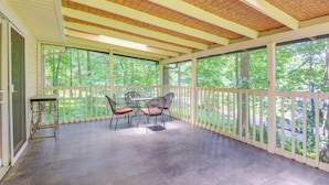 Un patio techado con mesa y sillas, un techo de pérgola y vista a árboles.