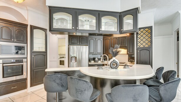 A modern kitchen with dark cabinetry, a stainless steel refrigerator, and a central island with bar stools.
