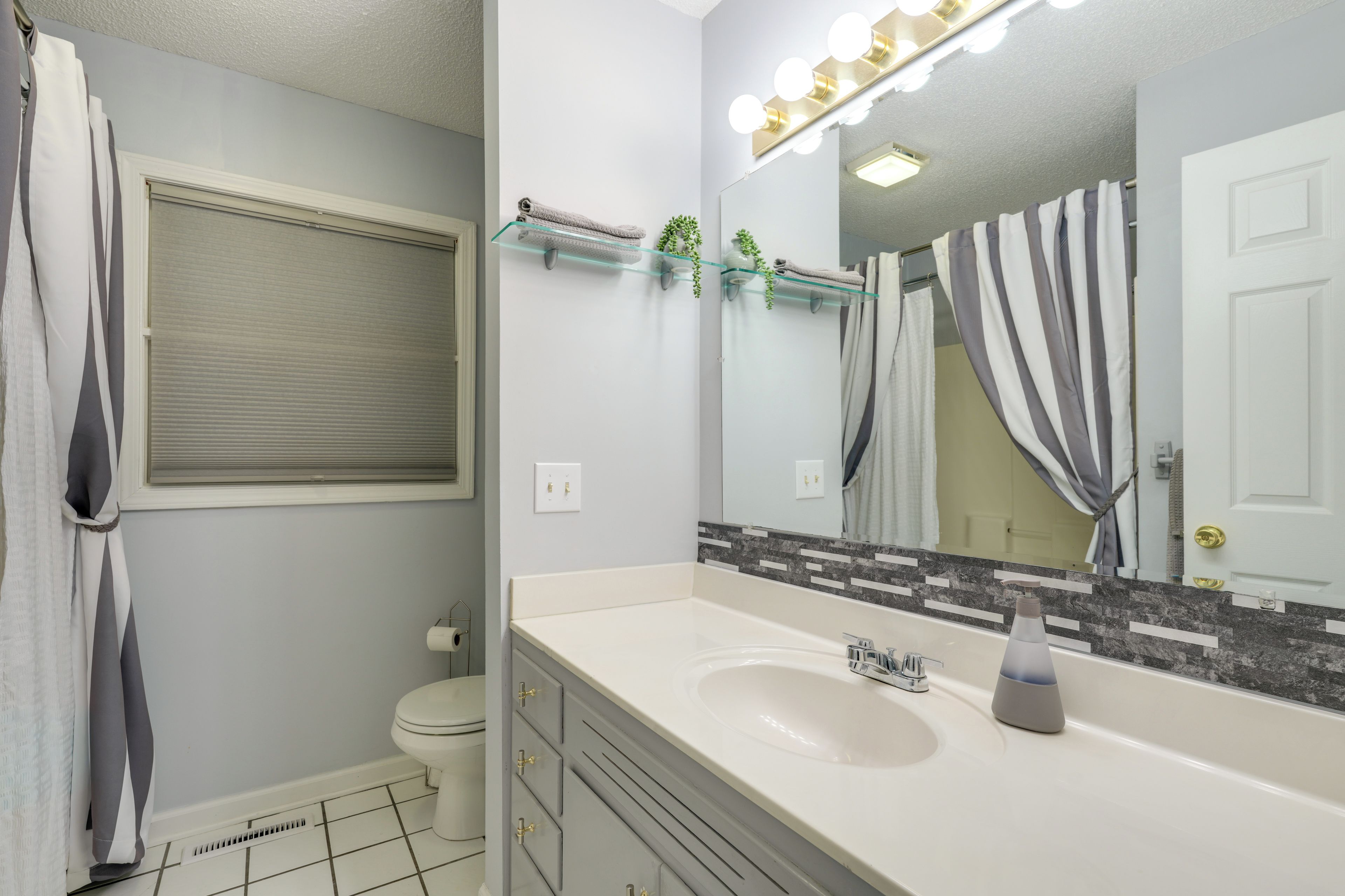 A bathroom with a white sink, a mirror with lights, a towel rack, and a toilet.