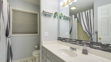 A bathroom with a white sink, a mirror with lights, a towel rack, and a toilet.