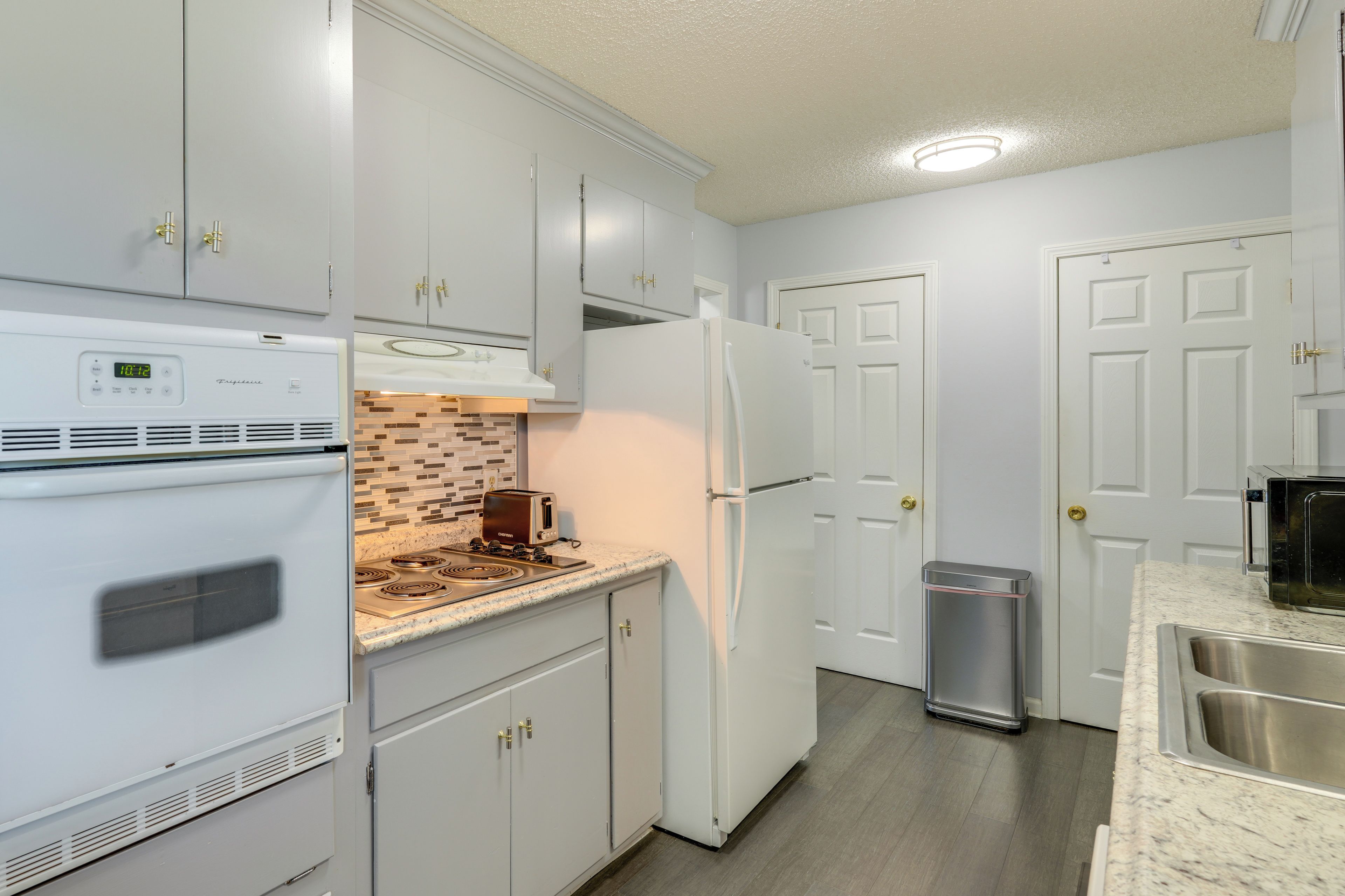 A kitchen with white cabinets, a built-in oven, a microwave, a toaster, and a stainless steel sink.