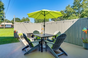 Une terrasse avec une table et des chaises, un parasol vert et une clôture en bois.