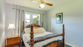 A four-poster bed with a wooden frame and a quilted bedspread, a bedside table with a lamp, and a ceiling fan.