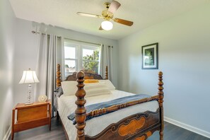 A four-poster bed with a wooden frame and a quilted bedspread, a bedside table with a lamp, and a ceiling fan. - Charming Kingsport Home w/ Spacious Fenced Yard! (Kingsport)