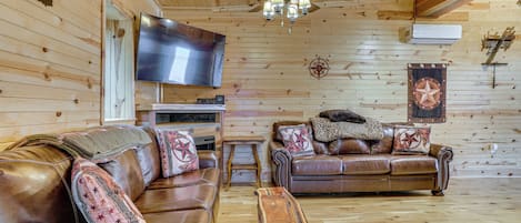 Una habitación con paneles de madera, sofás de cuero, una mesa de centro de madera, un ventilador de techo y un televisor de pantalla plana.