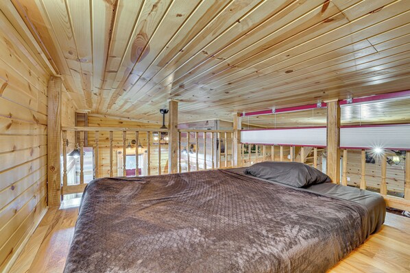 A wooden cabin interior with a bed, wooden walls, and a balcony with a red railing.