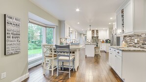 Une cuisine spacieuse avec des meubles blancs, un coin repas comprenant une table et des chaises en bois, et une vue sur l’extérieur grâce à de grandes fenêtres.