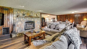 Ein gemütliches Wohnzimmer mit Kamin aus Stein, Holzvertäfelung, einer bequemen Couch und einem Essbereich mit Tisch und Stühlen.