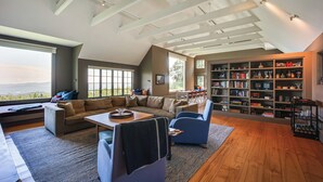 Een ruime woonkamer met een hoge plafond, een grote boekenkast en uitzicht op de omgeving.