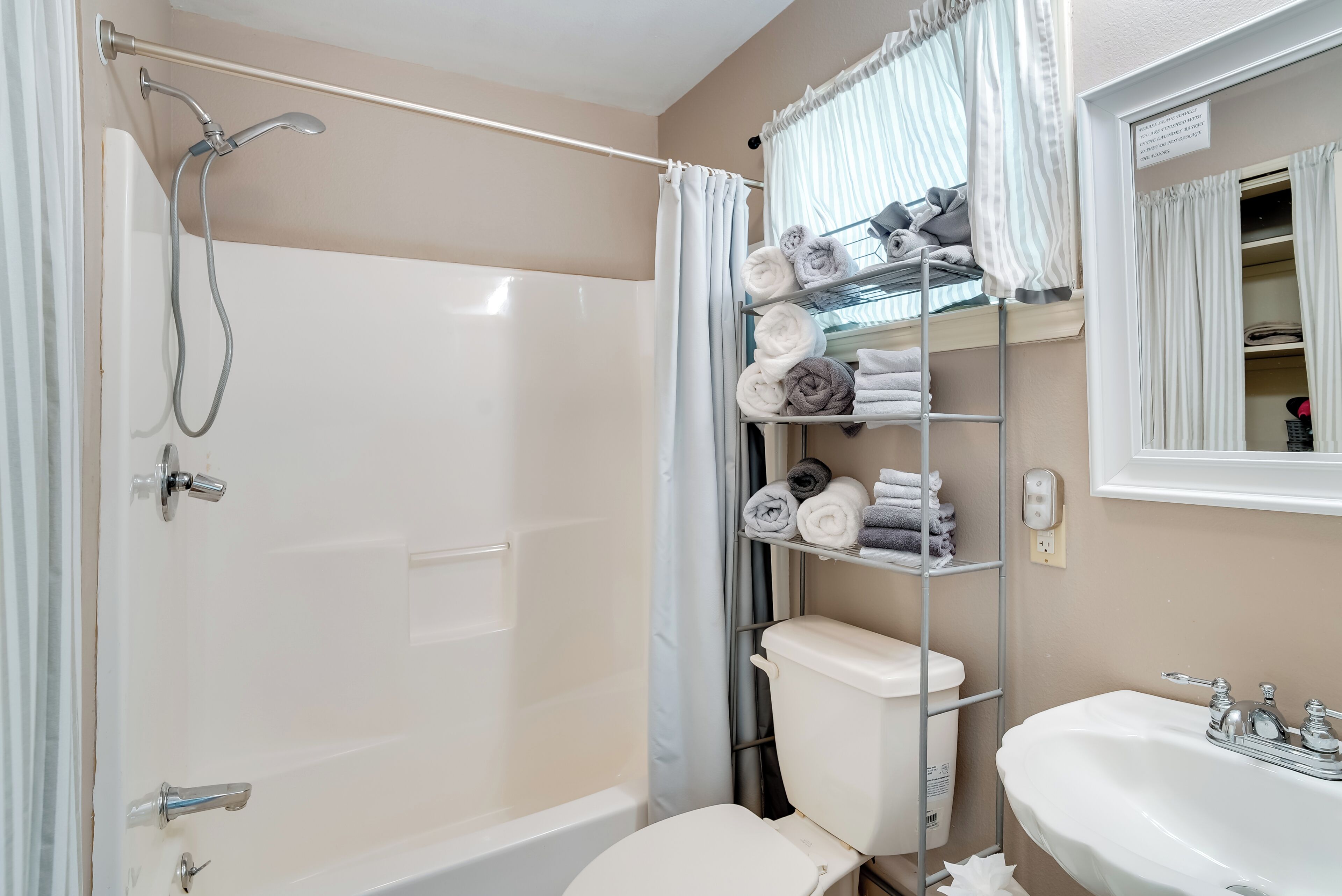 Baño con ducha, inodoro y lavabo. Hay toallas en un estante y un espejo sobre el lavabo.