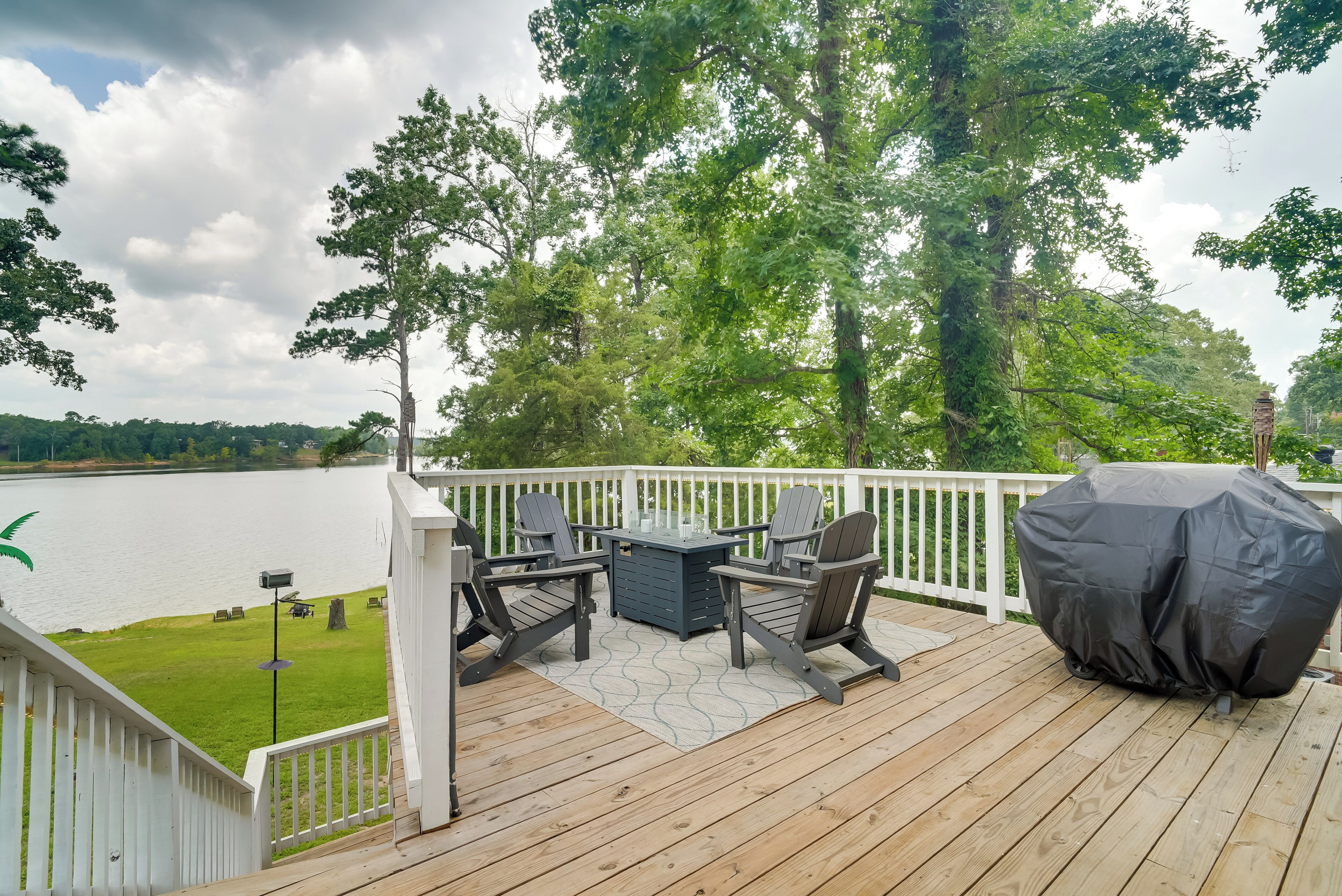 A deck with outdoor furniture, a grill, and a view of a lake.