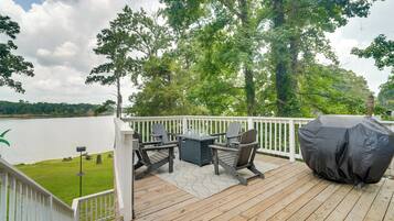 A deck with outdoor furniture, a grill, and a view of a lake.