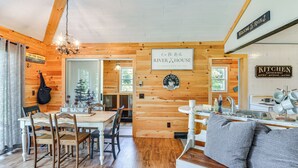 Un intérieur chaleureux, aménagé dans le style d’un chalet, avec un coin repas en bois, une cuisine où est affiché un panneau indiquant «Espace convivial de la cuisine» et un panneau accueillant les visiteurs à la «Maison River X».
