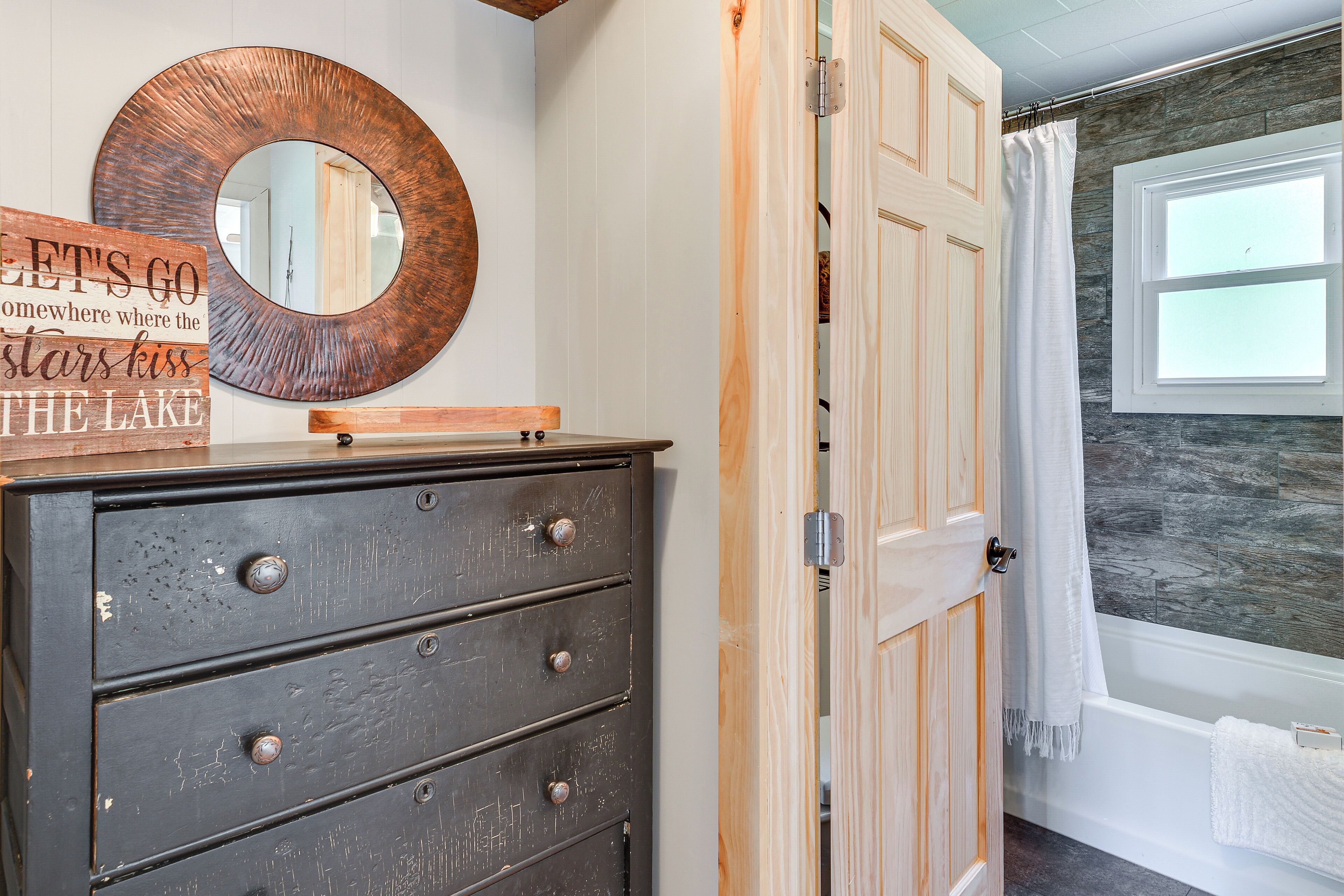 A bathroom with a bathtub, a wooden door, and a mirror on the wall.