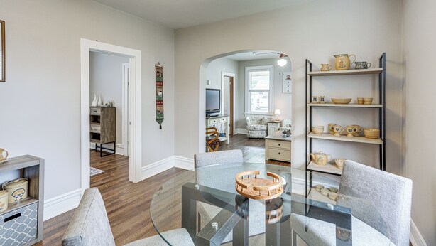 Een moderne woonkamer met een glazen salontafel, grijze banken en een houten bijzettafeltje. Er is een boekenkast met decoratieve objecten en een televisie op de achtergrond.