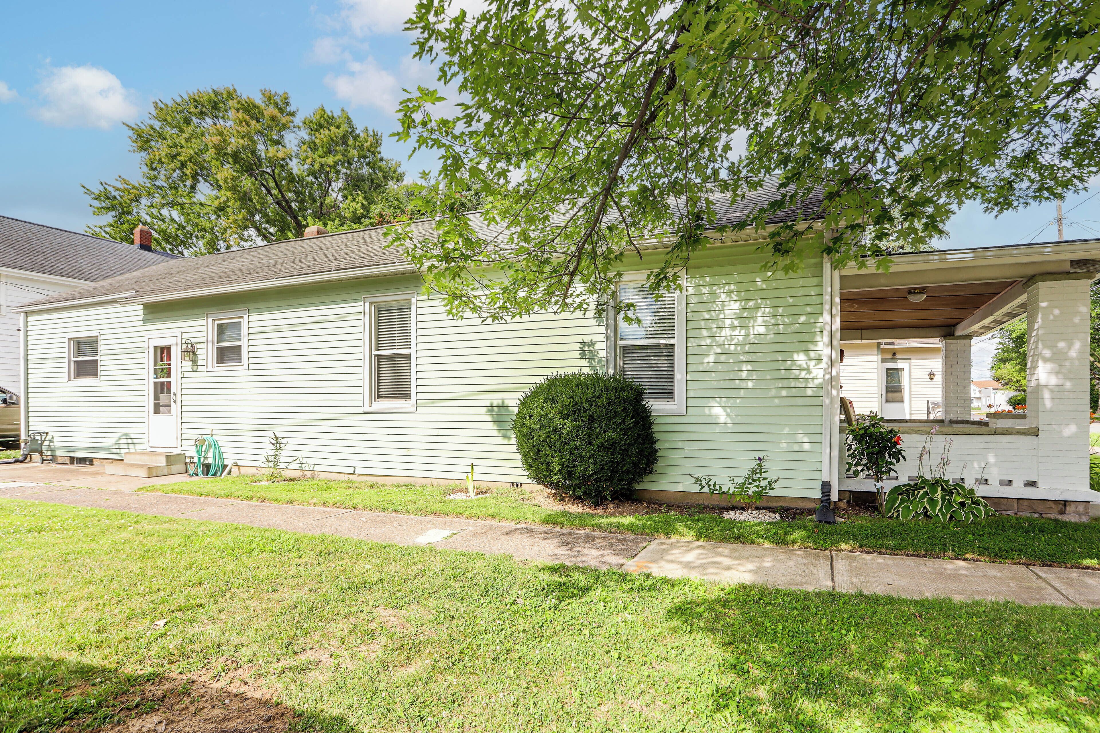 A single-story house with a front porch, a small front yard, and a tree providing shade.