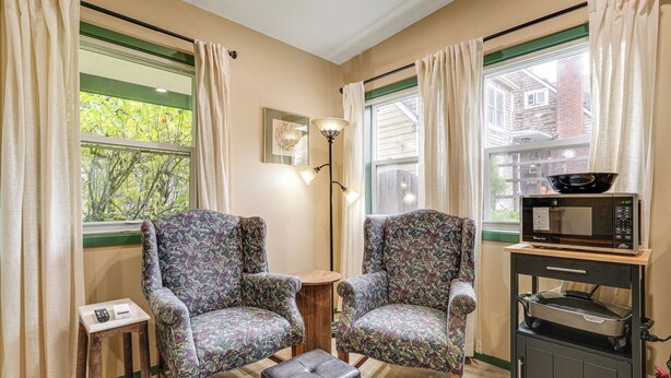 A cozy living room with two patterned armchairs, a small wooden table, a black ottoman, a floor lamp, a microwave, and a cart with a grill. - < 1/2 Mi to Osu: Studio in Corvallis Near Parks (Corvallis)