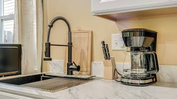 A kitchen with a modern coffee maker, a sink with a faucet, and a window with curtains.
