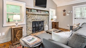 A living room with a stone fireplace, a mounted TV, and a cozy seating area. - Hot Tub + Deck: Cabin Hideaway in Brown County (Nineveh)
