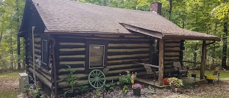 A rustic log cabin with a chimney, a porch, and a wheelbarrow.