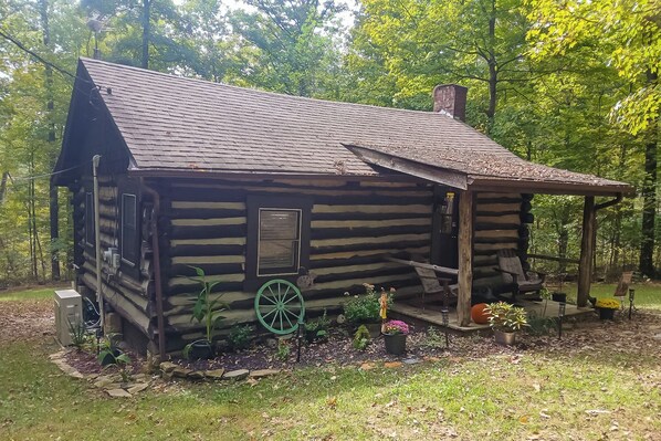A rustic log cabin with a chimney, a porch, and a wheelbarrow. - Hot Tub + Deck: Cabin Hideaway in Brown County (Nineveh)